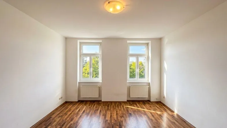 Helles Zimmer mit zwei Fenstern und schönem Parkettboden, ideal als Wohn- oder Schlafzimmer.
