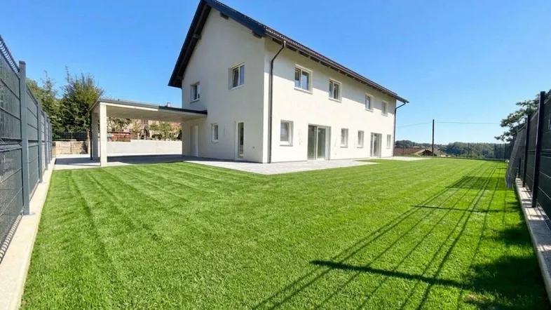Modernes Einfamilienhaus mit großem, gepflegtem Rasen und Carport unter blauem Himmel.