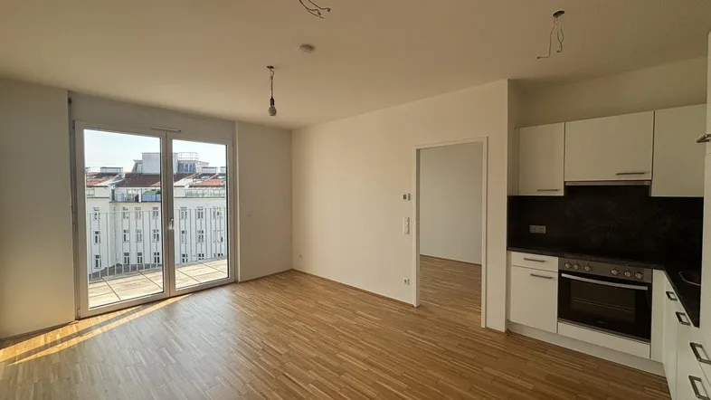 Heller Wohn- und Küchenbereich mit Parkettboden und Zugang zu einem Balkon, ideal für offenes Wohnen.