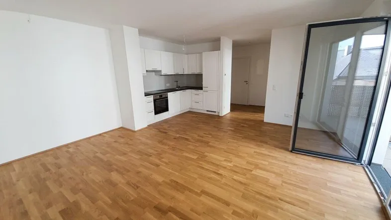 Helles Wohnzimmer mit offener Küche, Parkettboden und Zugang zum Balkon.