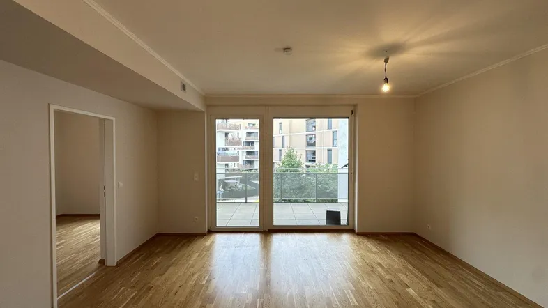 Helles Wohnzimmer mit Holzboden und Zugang zu einem Balkon mit Blick auf moderne Gebäude.