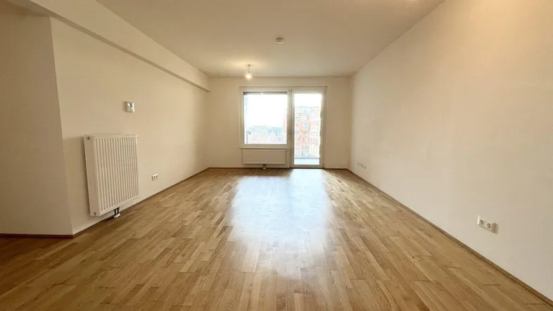 Helles, leeres Wohnzimmer mit Parkettboden und Zugang zu einem Balkon, bereit zur individuellen Gestaltung.