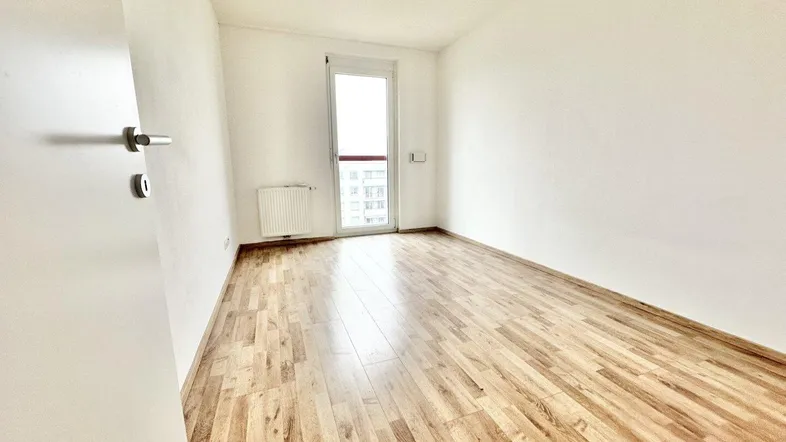 Helles, leeres Zimmer mit Laminatboden und Zugang zu einem Balkon oder einer Loggia.