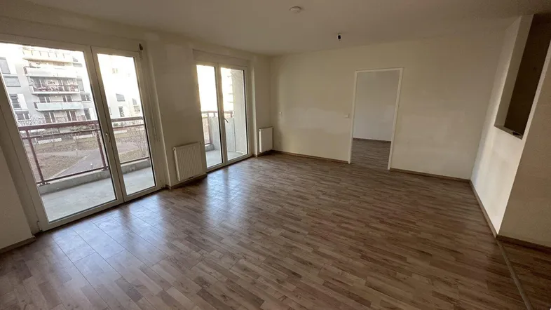 Heller, unmöblierter Wohnraum mit Holzboden und Zugang zu einem Balkon.