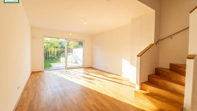 Helles Wohnzimmer mit Holzboden, Zugang zur Terrasse und offener Treppe.