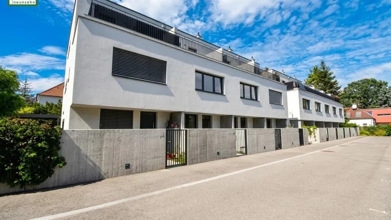 Moderne Reihenhäuser mit weißer Fassade, dunklen Fenstern und Balkonen unter blauem Himmel.
