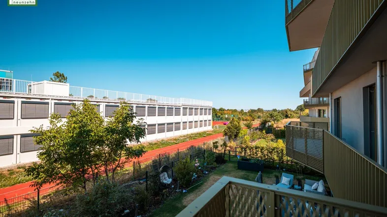 Blick vom Balkon auf eine Sportanlage, grüne Umgebung und ein angrenzendes modernes Gebäude.