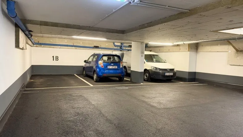 Geräumige Tiefgarage mit mehreren Stellplätzen und sichtbaren Installationen an der Decke.