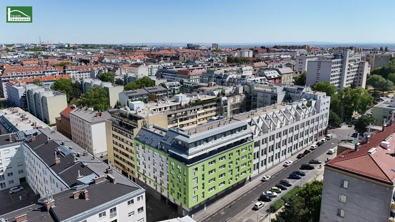 Luftaufnahme einer städtischen Umgebung mit Wohngebäuden und einer weiten Stadtsilhouette im Hintergrund.