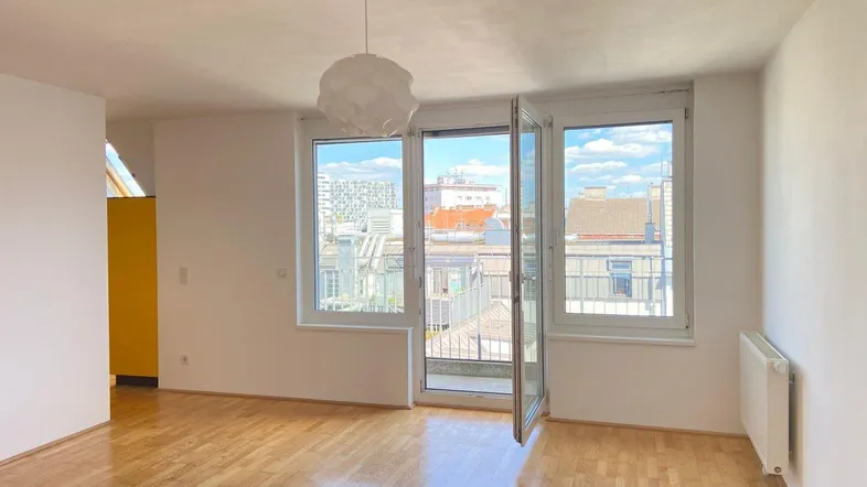 Helles Zimmer mit Parkettboden, großen Fenstern und Zugang zu einem kleinen Balkon.
