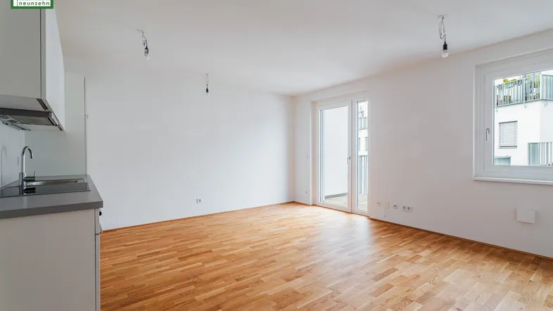 Heller offener Wohnbereich mit Parkettboden, weißen Wänden und Zugang zum Balkon.