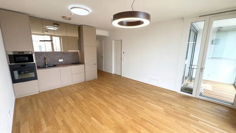 Heller Wohnbereich mit Parkettboden, integrierter Küchenzeile und Zugang zu einem Balkon.