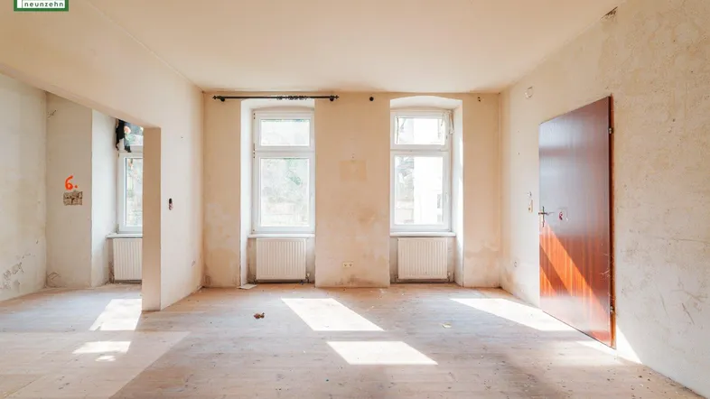Heller, leerer Raum mit Holzdielenboden und zwei Fenstern, bereit zur Renovierung.