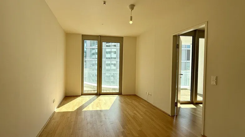 Helles Wohnzimmer mit Holzboden und Zugang zu einem Balkon, bietet viel natürliches Licht.