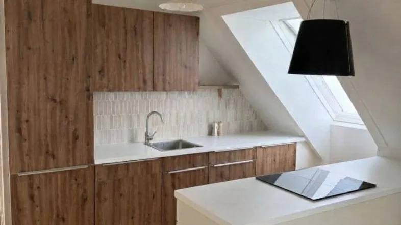 Moderne Küche mit Holzfronten, weißer Arbeitsplatte, Kochinsel und Dachfenster unter einer Dachschräge.