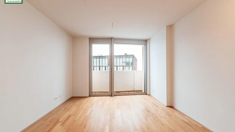 Helles Zimmer mit Holzboden und Zugang zu einem Balkon, ideal als Wohn- oder Schlafbereich.