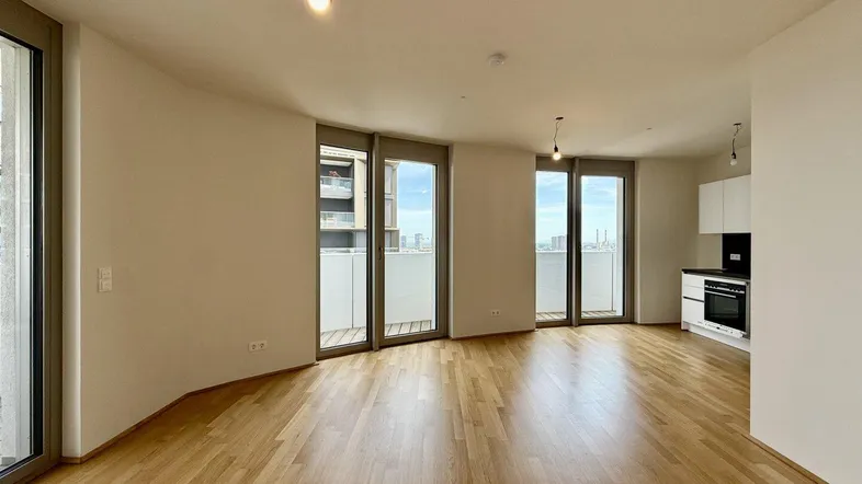 Helles Wohnzimmer mit integrierter Küchenzeile, Parkettboden und großen Fenstern mit Stadtblick.