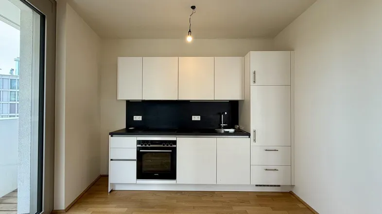 Moderne Einbauküche in Weiß mit dunkler Arbeitsplatte und Zugang zum Balkon.