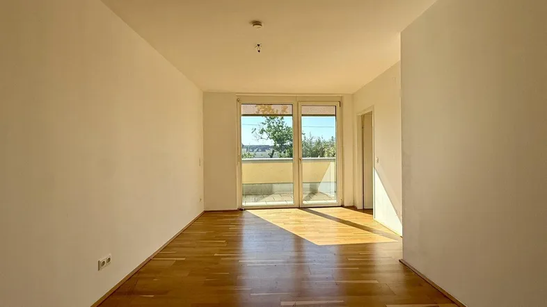 Helles Zimmer mit Parkettboden und Zugang zu einem Balkon, ideal als Wohn- oder Schlafbereich.