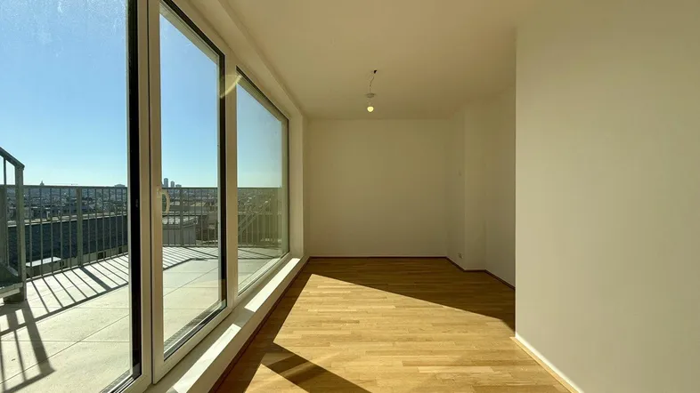 Helles Zimmer mit Holzboden und großen Fenstern, die viel Tageslicht hereinlassen und einen weiten Blick bieten.