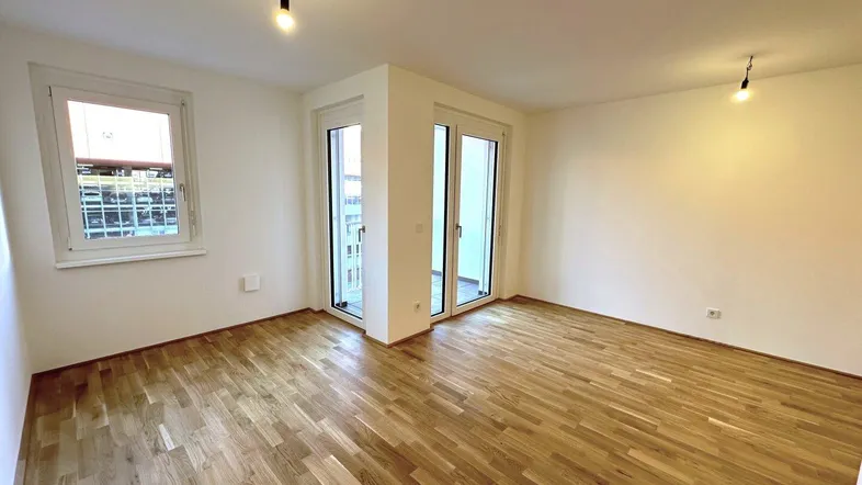 Helles, leeres Zimmer mit Parkettboden und Zugang zu einem Balkon, ideal als Wohnbereich.