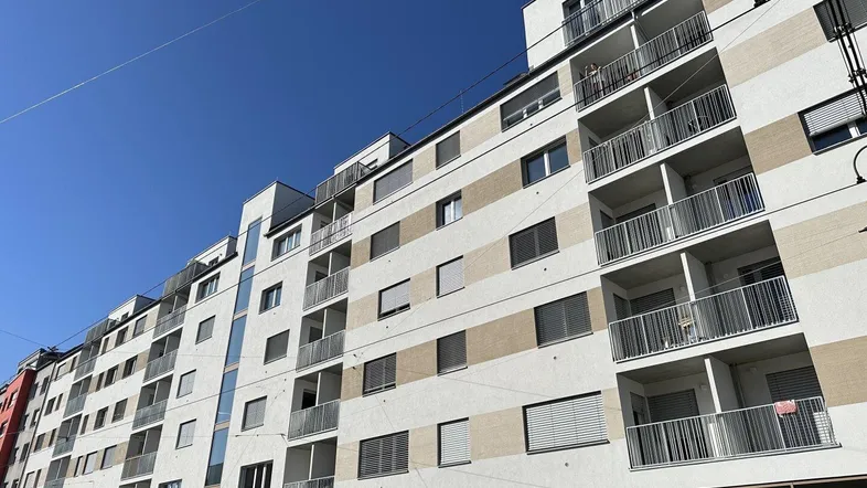 Moderne Wohnhausfassade mit Balkonen und großen Fenstern unter blauem Himmel.