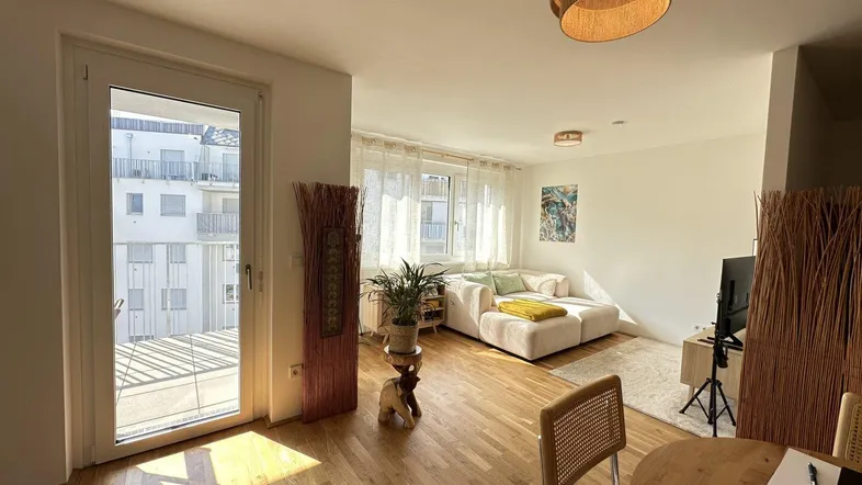 Helles Wohnzimmer mit Holzboden, Sofa und Zugang zu einem Balkon, modern eingerichtet.