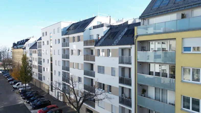 Moderne Wohngebäude mit Balkonen und Parkplätzen an einer städtischen Straße.