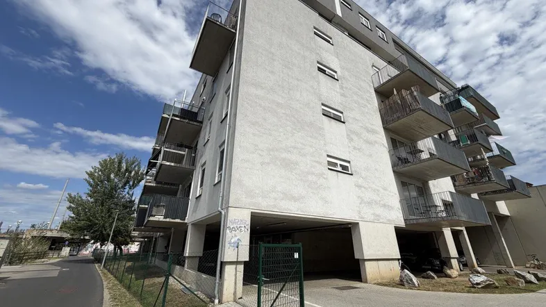 Modernes Mehrfamilienhaus mit Balkonen und Zugang zur Tiefgarage unter blauem Himmel.