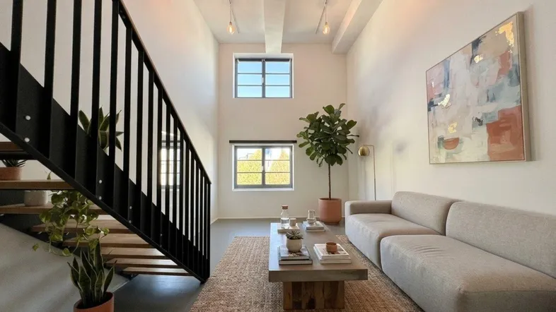 Helles Wohnzimmer mit hohen Decken, modernen Möbeln und einer eleganten Treppe.