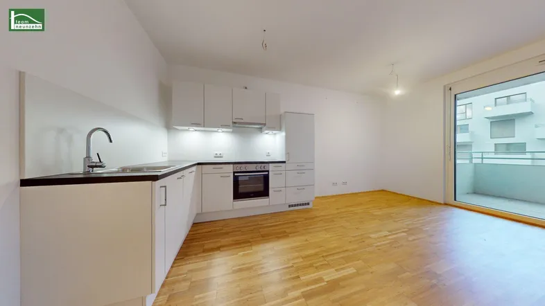 Moderne Einbauküche mit weißen Schränken und Holzboden, offen zum Wohnbereich mit Balkonzugang.