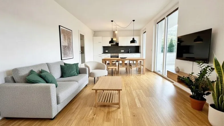 Helles, offenes Wohnzimmer mit integriertem Essbereich und moderner Küche, ausgestattet mit Holzboden und großen Fenstern.
