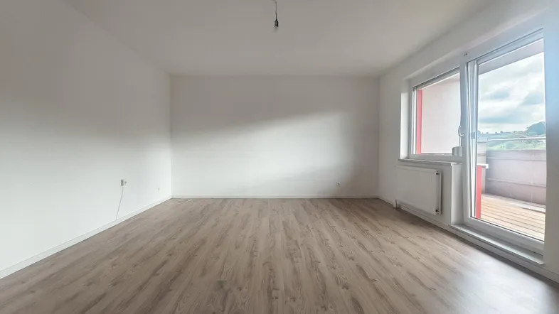 Helles, leeres Zimmer mit Laminatboden und Zugang zu einem Balkon, ideal für Wohn- oder Schlafbereich.