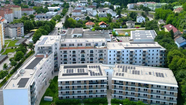 Luftaufnahme moderner Wohngebäude mit Solaranlagen auf den Dächern in einer grünen Umgebung.