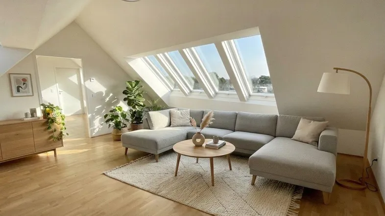 Helles, modern eingerichtetes Wohnzimmer im Dachgeschoss mit großen Dachfenstern und Holzboden.