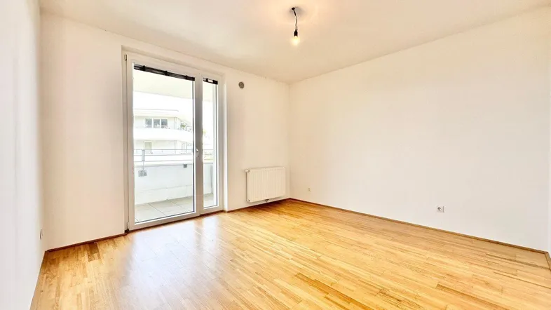 Helles Zimmer mit Parkettboden und Zugang zu einem Balkon, ideal als Wohn- oder Schlafzimmer.