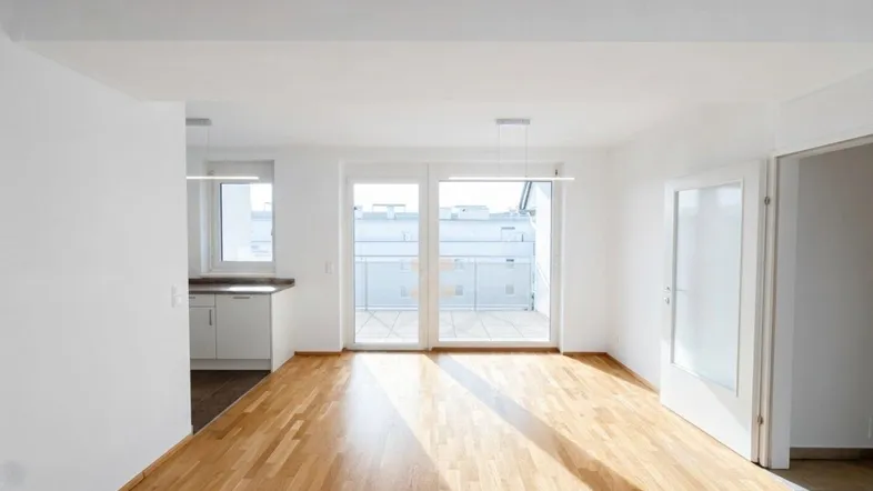 Helles Wohnzimmer mit Parkettboden und Zugang zu einem Balkon oder einer Terrasse.
