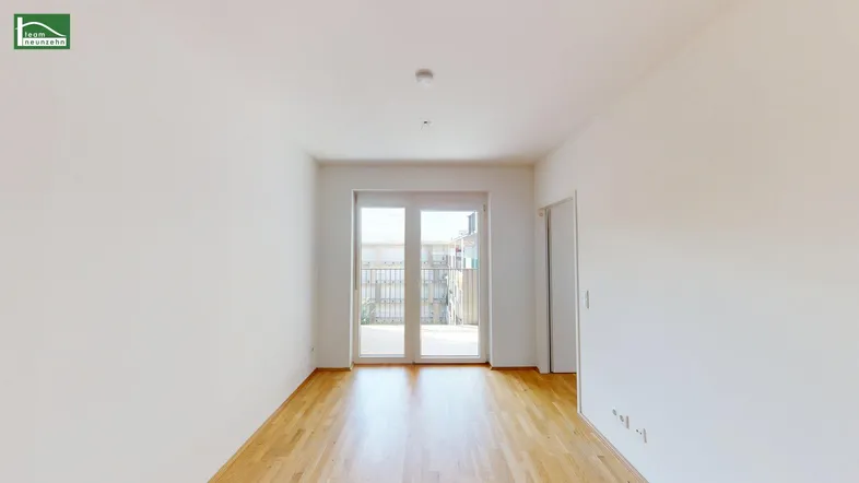 Helles, leeres Wohnzimmer mit Parkettboden und Zugang zu einem Balkon.