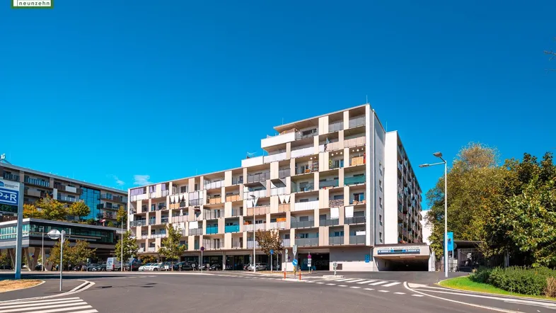 Modernes Mehrfamilienhaus mit zahlreichen Balkonen und einer belebten Straße im Vordergrund.