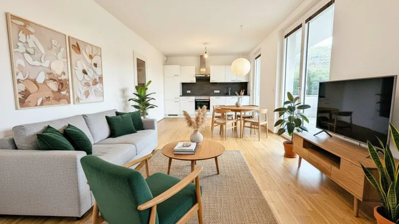 Helles, modern eingerichtetes Wohnzimmer mit offener Küche, Essbereich und Zugang zu großen Fenstern.