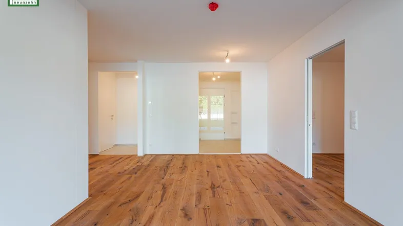 Heller Innenraum mit Holzboden und Durchgängen zu weiteren Zimmern in einem Neubau.