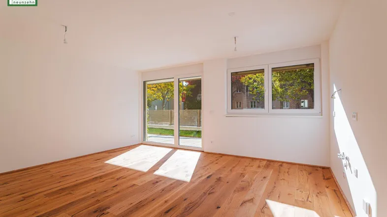 Helles, leeres Zimmer mit Holzboden und Zugang zu einem Außenbereich, durchflutet von Sonnenlicht.