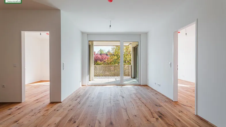 Heller, leerer Wohnbereich mit Holzboden und Zugang zu einem sonnigen Balkon.