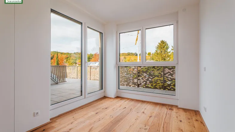 Heller Raum mit Holzboden und großen Fenstern, die Zugang zu einer Terrasse bieten.