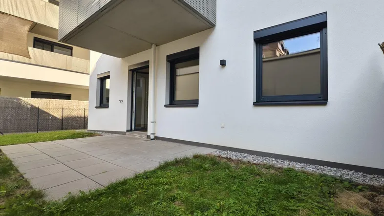 Gepflasterte Terrasse mit angrenzendem Rasenfläche und Zugang zum modernen Gebäude mit Balkon.