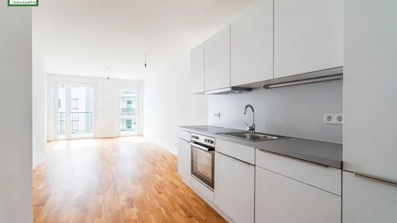 Heller Wohnbereich mit moderner Küchenzeile, Parkettboden und Zugang zum Balkon.