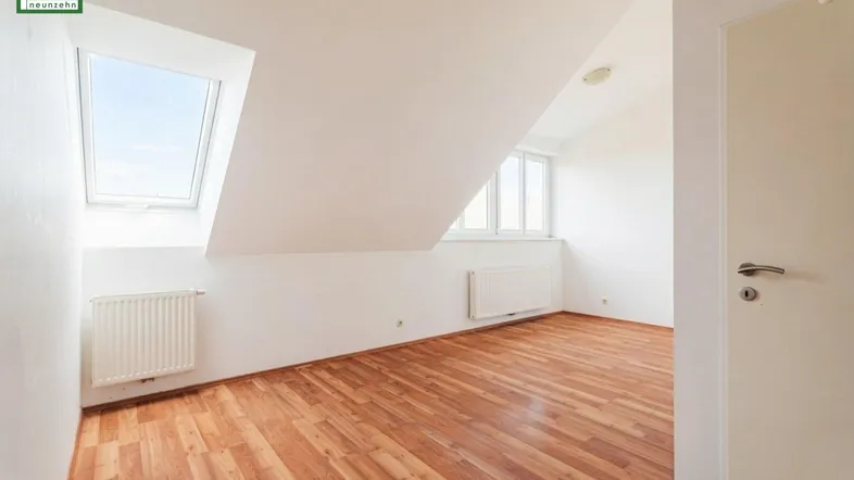 Helles Zimmer im Dachgeschoss mit Dachfenster, Schrägdecke und Parkettboden.