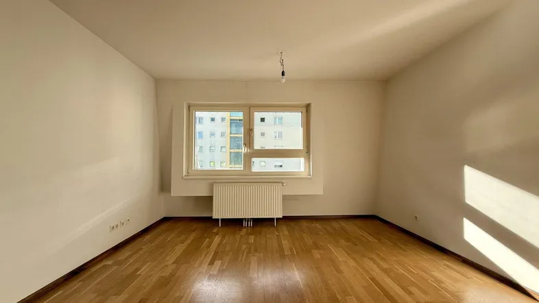 Helles, leeres Zimmer mit Parkettboden und großem Fenster, bereit zur individuellen Gestaltung.