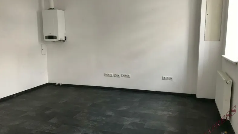 Leerer Raum mit weiß gestrichenen Wänden, dunklem Fliesenboden und Heizungsanlage an der Wand.