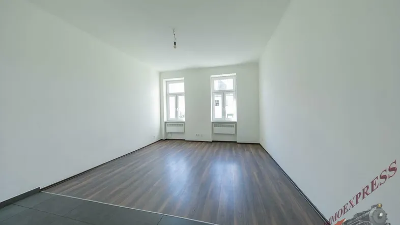 Helles, leeres Zimmer mit dunklem Laminatboden und weißen Wänden, bereit zur Einrichtung.